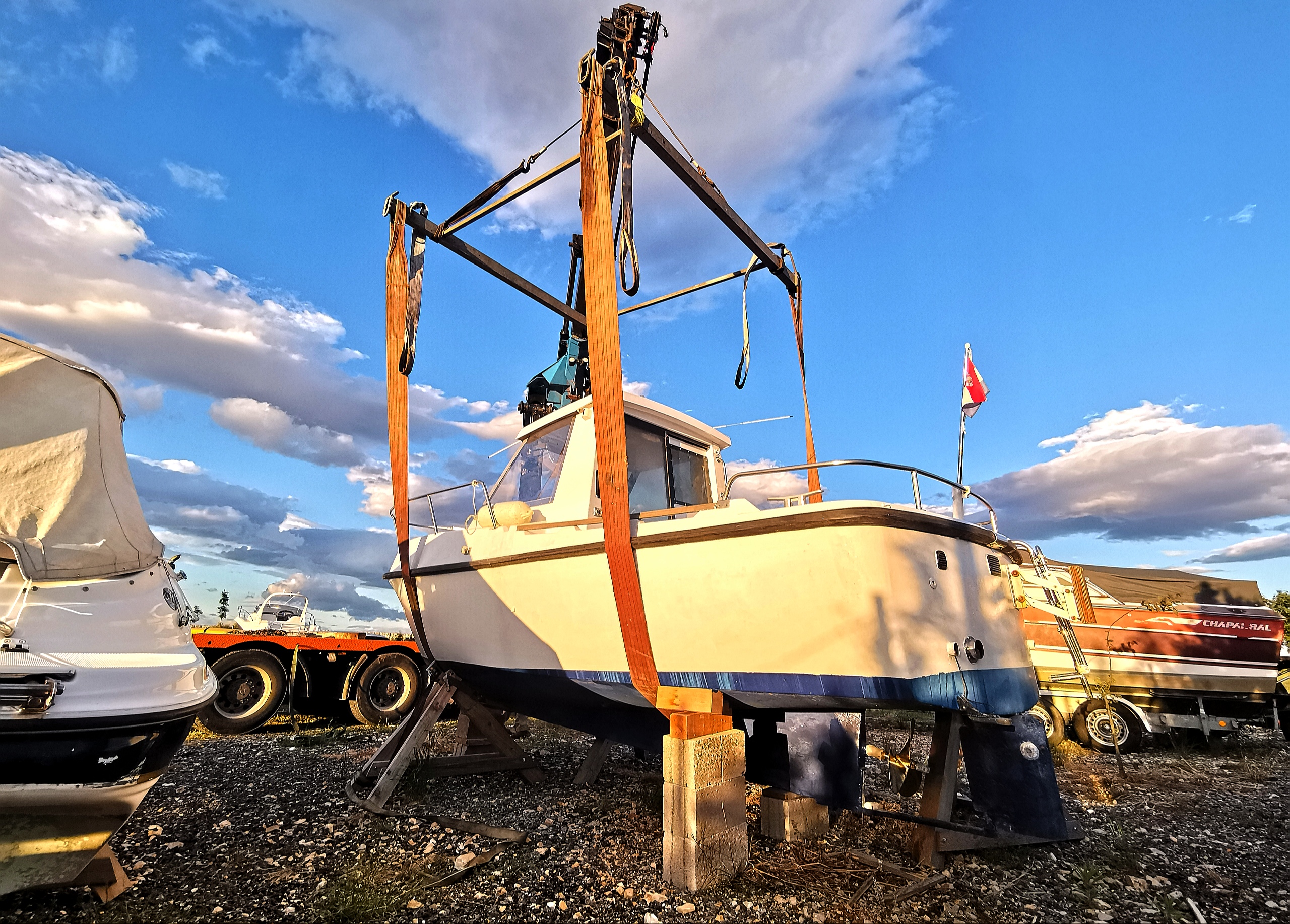 Cabin boat standing on blocks in lifting slings in the Eurotransporti dry marina at sunset