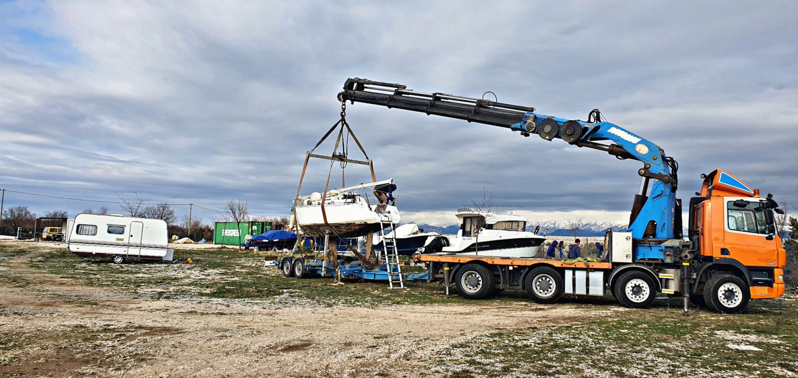 Orange Eurotransporti crane truck lifting a sailboat onto a trailer in the boat yard