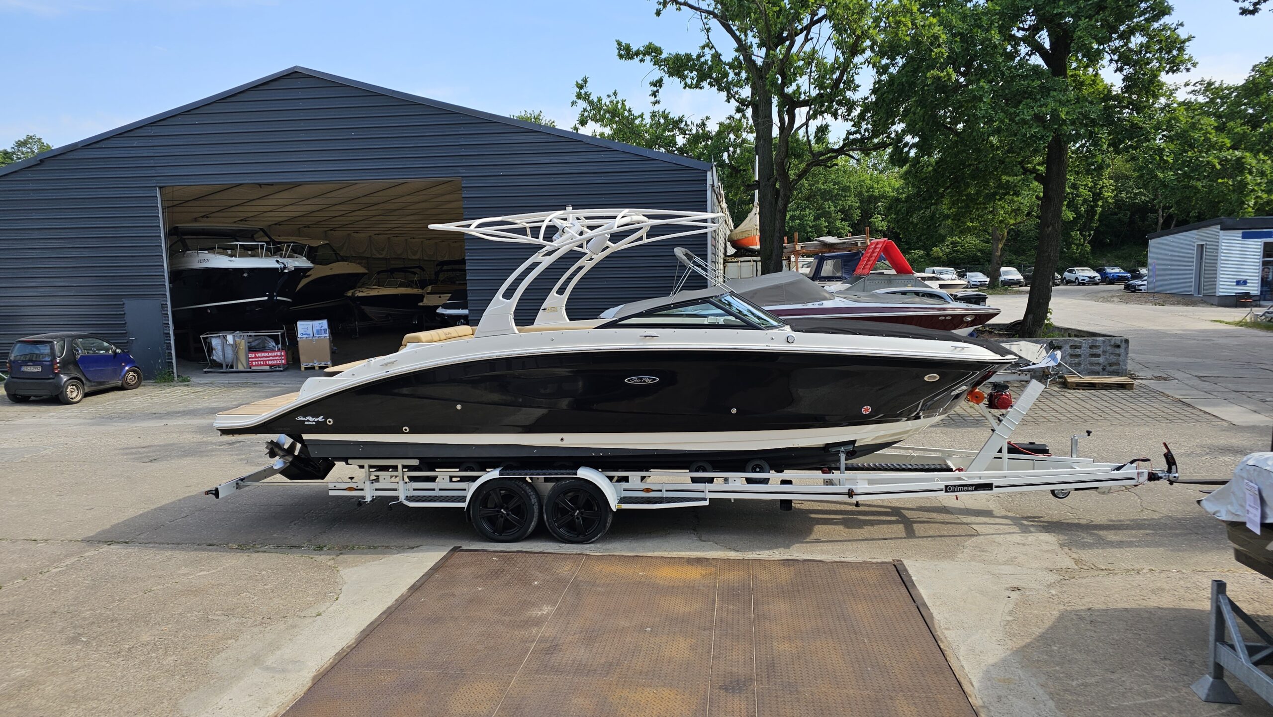 Black and white sport boat on trailer in front of a storage hall ready for road transport