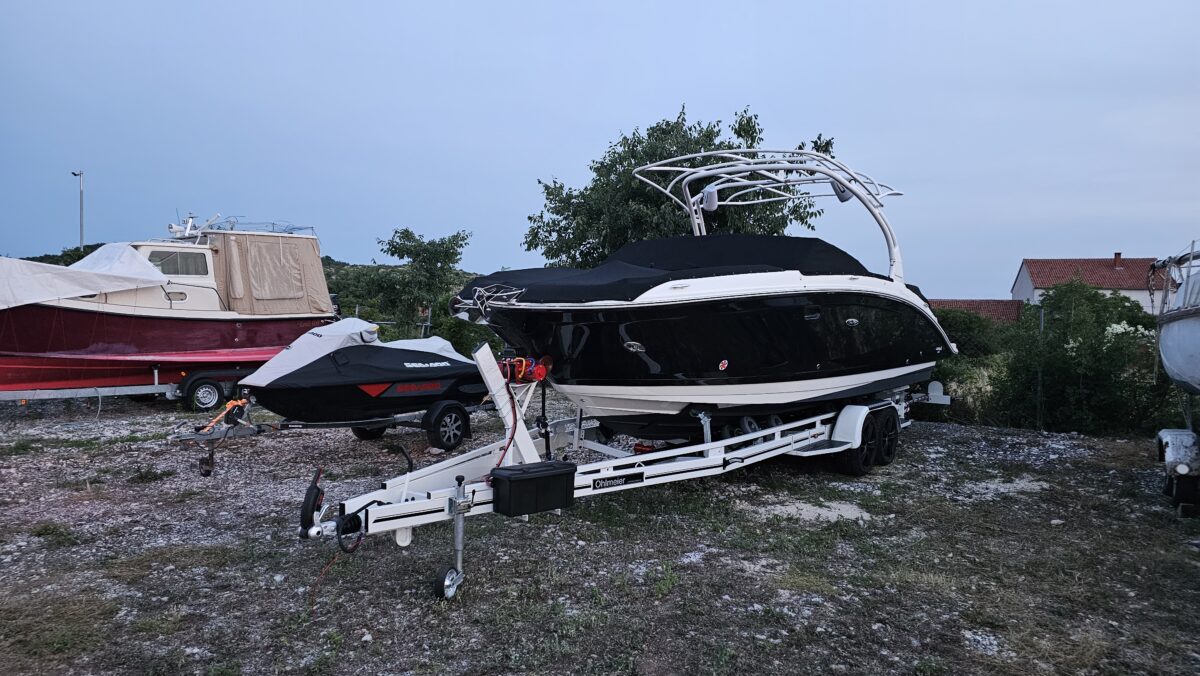 Black sport boat on Ohmleier trailer and Sea-Doo jet ski stored in the Eurotransporti dry marina yard at evening