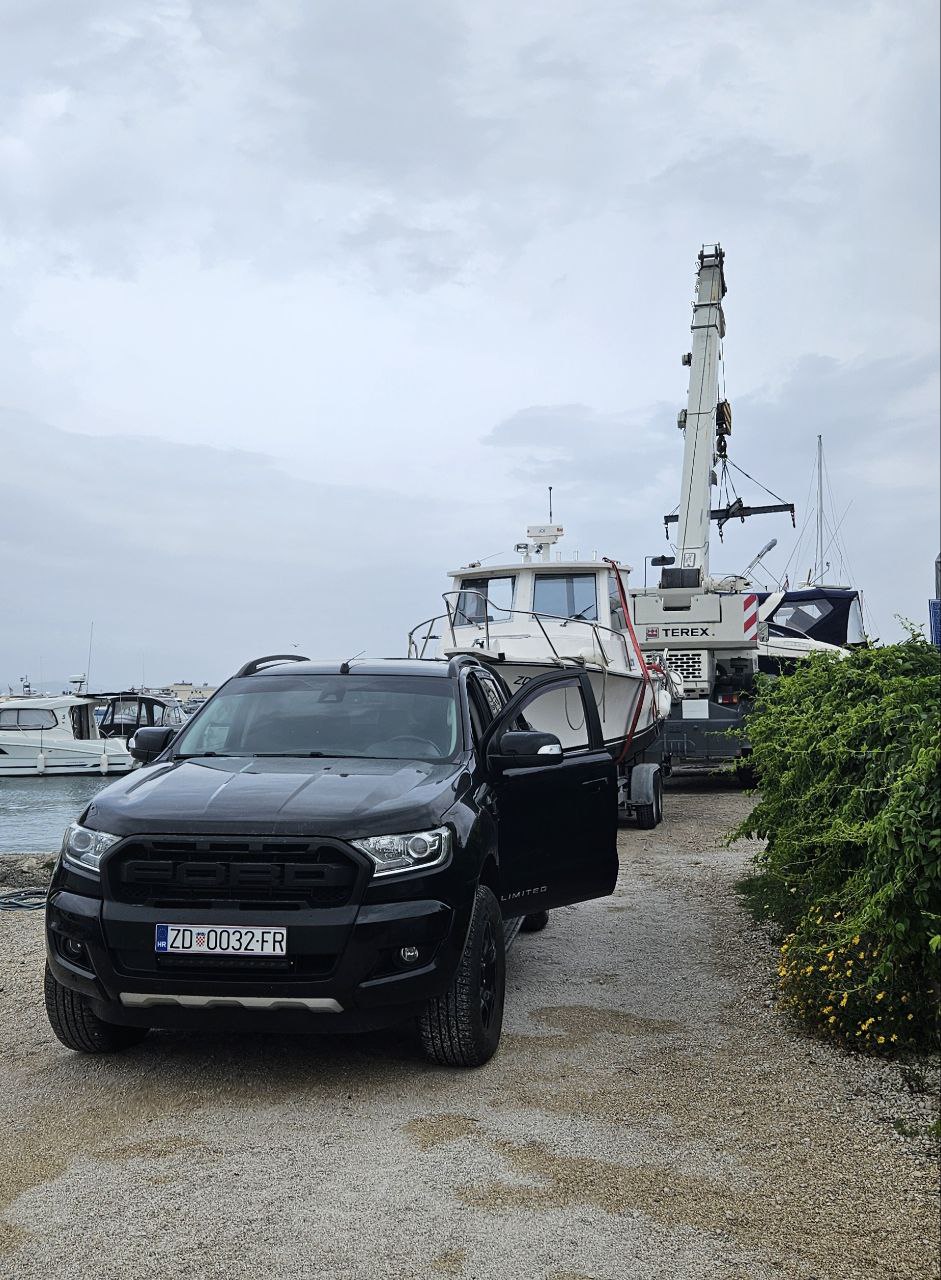 Ford Ranger pickup parked beside a crane lifting a boat at the marina on a cloudy day
