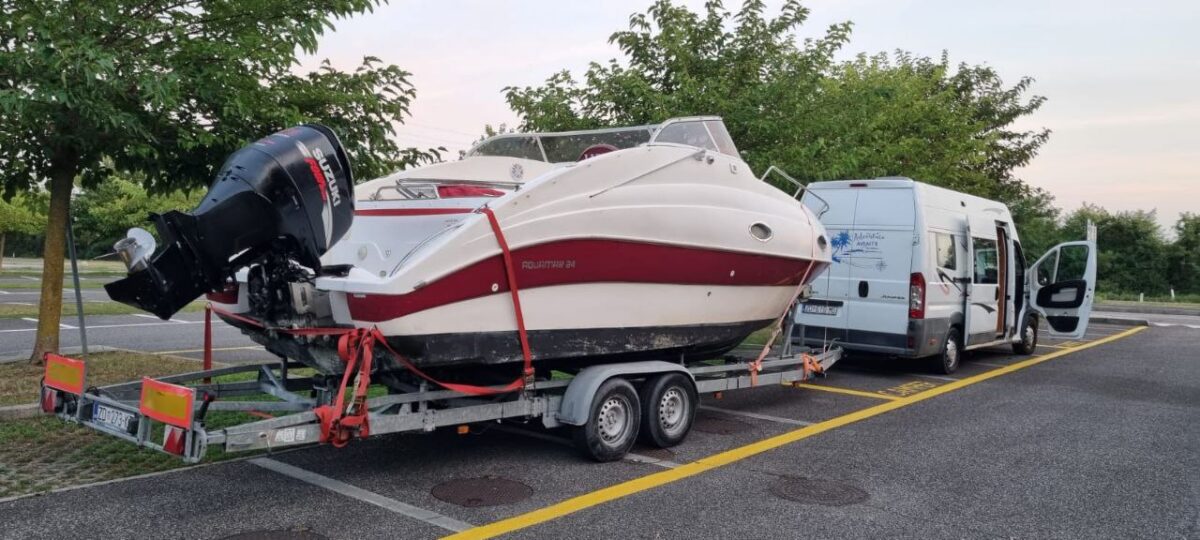 Aquamar 21 boat secured on a twin-axle trailer being transported by a white van during a professional marine transport service