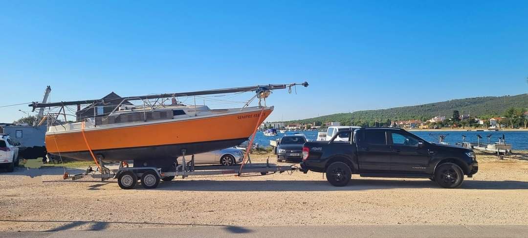 Black pickup towing the sailing yacht Sempre Felice on a dual-axle boat trailer during professional yacht transport services