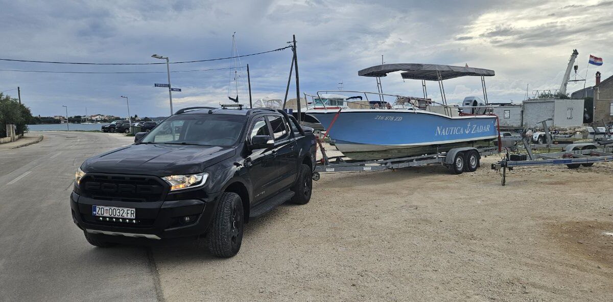 Black Ford Ranger towing a blue Nautica Zadar boat on a trailer at the waterfront
