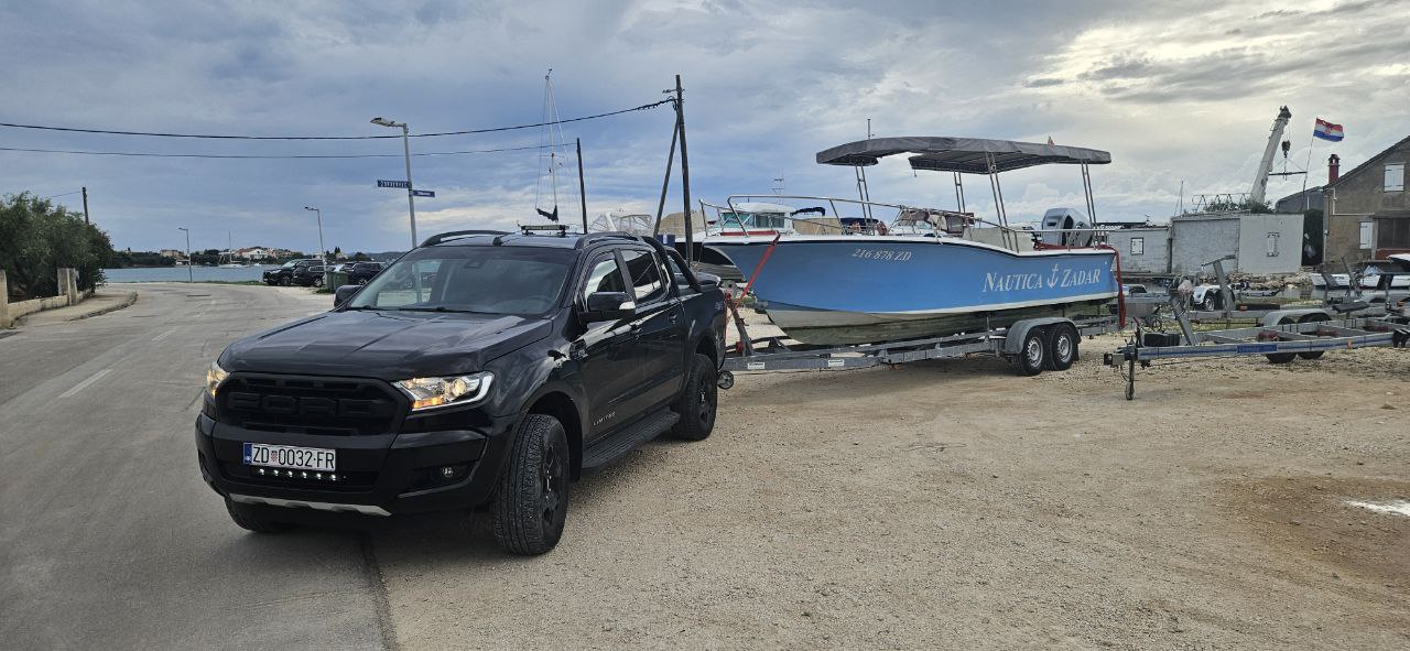 Black Ford Ranger towing a blue Nautica Zadar boat on a trailer at the waterfront