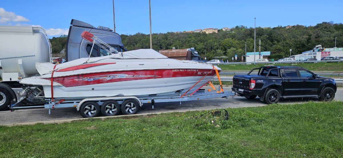 Black Ford Ranger towing a large red and white motorboat on a triple-axle trailer at a highway rest stop